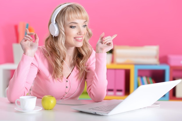 Mooie jonge vrouw in koptelefoon met laptop in kamer met roze muren