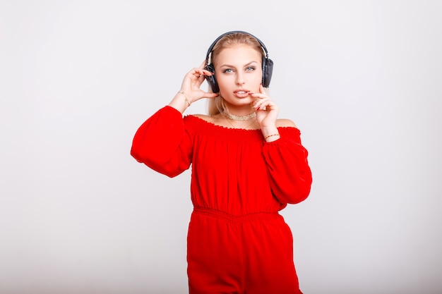 Mooie jonge vrouw in modieuze rode kleding met koptelefoon luisteren muziek op grijs