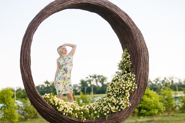 Mooie jonge vrouw in mooie jurk poseren op kleurrijke muur van bloemen. Modefoto, mooi haar, grote glimlach