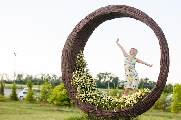 Mooie jonge vrouw in mooie jurk poseren op kleurrijke muur van bloemen. Modefoto, mooi haar, grote glimlach