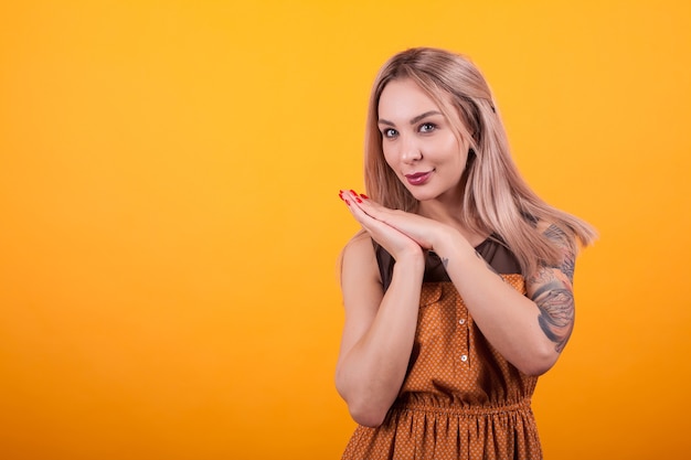 Mooie jonge vrouw in oranje jurk glimlachend over gele achtergrond. Tatoeage op haar armen. Vrolijke jonge vrouw.