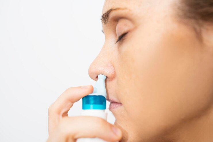 Mooie jonge vrouw in profiel die zeewater sinus medicijn aanbrengt voor slijm schoonmaak neus