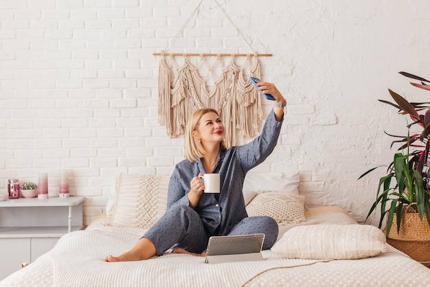 Foto mooie jonge vrouw in pyjama die aan een laptop in bed werkt en aan de telefoon praat online winkelen