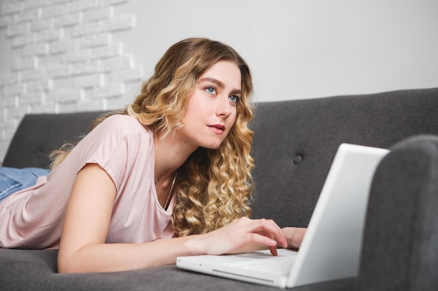 Mooie jonge vrouw in roze shirt die op de laptop werkt Meisje liggend op de bank met notebook Dis