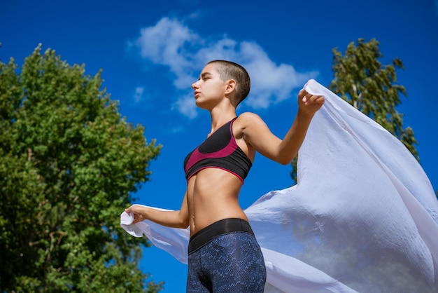 Mooie jonge vrouw in sportkleding mediteren in de natuur met haar armen gespreid