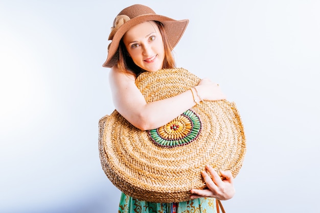 Mooie jonge vrouw in strand hoed zomerjurk knuffelen een rotan strandtas. concept liefde voor zomerstrand