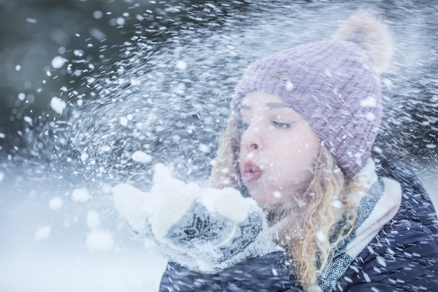 Mooie jonge vrouw in warme kleding waait sneeuw.