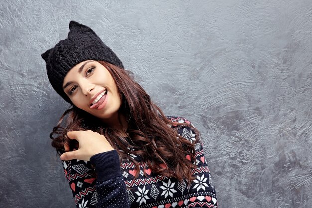 Foto mooie jonge vrouw in warme kleren die zich dichtbij grijze getextureerde muur bevindt