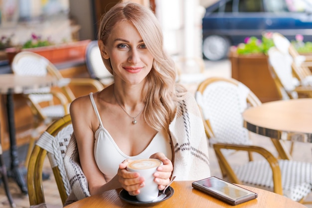 Mooie jonge vrouw in warme plaid in een terrasje aan tafel drinken