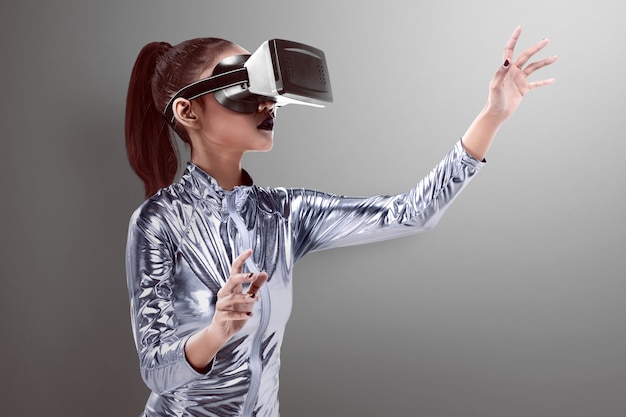 Mooie jonge vrouw in zilveren latexkostuum en VR-hoofdtelefoon