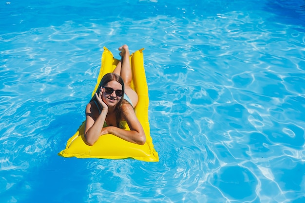 Mooie jonge vrouw in zonnebril op een gele opblaasbare matras in een zwembroek zwemt in het zwembad van een luxe hotel zomervakantie reizen smile