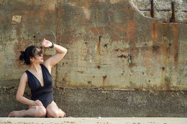 Foto mooie jonge vrouw in zwart zwembroek poseert tegen de achtergrond van oude roestige betonnen muur op