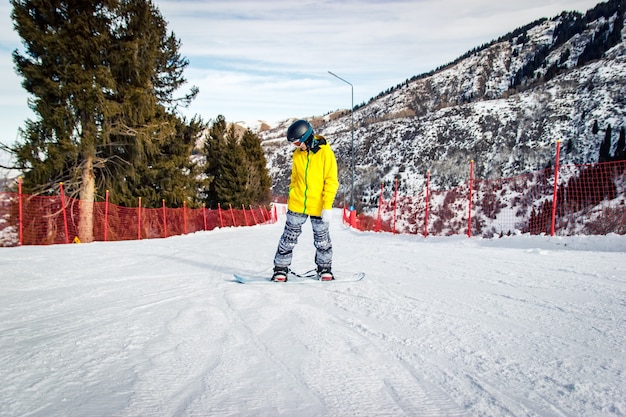 Foto mooie jonge vrouw in zwarte helm en gele jas leert teen kant rijden op snowboard