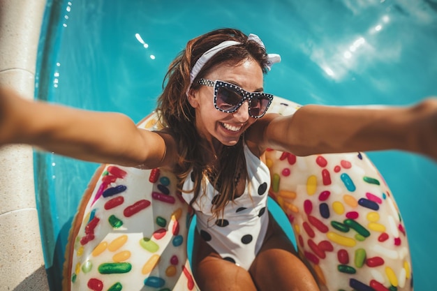 Mooie jonge vrouw in zwembad zwemt op opblaasbare ring donut en heeft plezier bij het maken van selfie in water op vakantie.