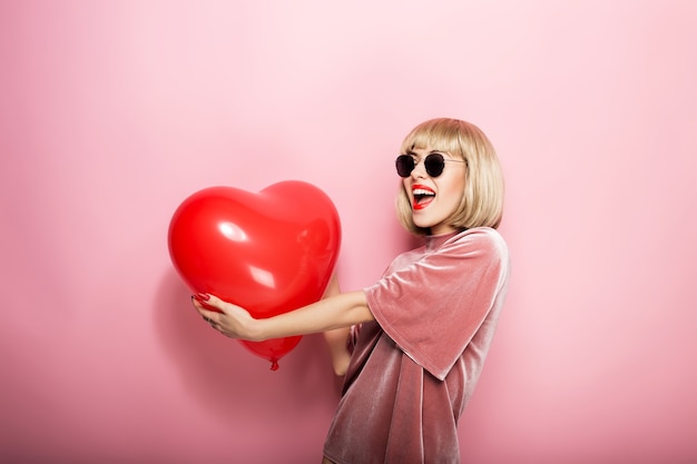 Mooie jonge vrouw knuffelen in de vorm van een hart rode bal en glimlachen. Op een roze achtergrond.