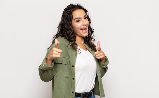 Mooie jonge vrouw lachend met een positieve, succesvolle, gelukkige houding wijzend naar de camera, pistool teken met handen maken