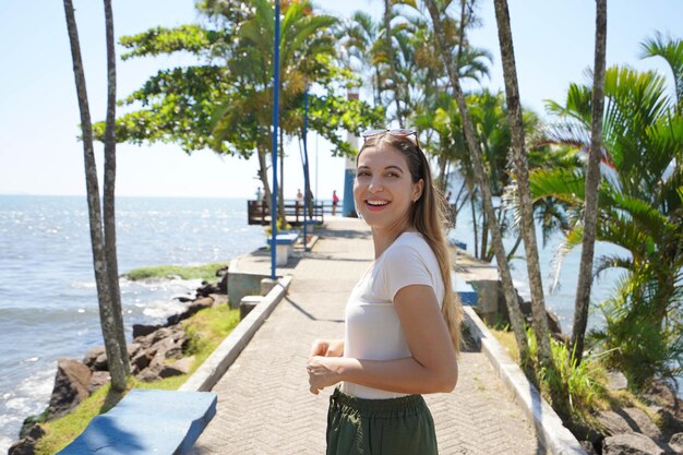 Foto mooie jonge vrouw loopt op de promenade van ubatuba met de vuurtoren farol do cruzeiro costa verde brazilië