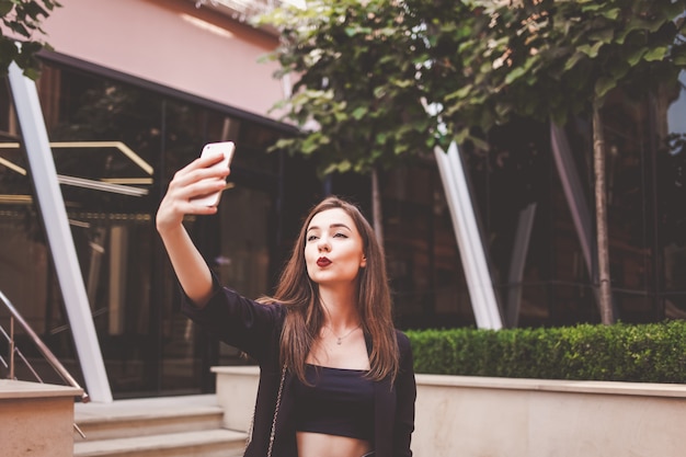 Mooie jonge vrouw maakt selfie op de achtergrond van een modern gebouw