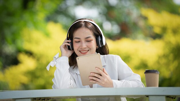 Mooie jonge vrouw meisje in beige shirt poseren in groene stad Park achtergrond glimlach meisje luisteren muziek met koptelefoon gevoel aanraken geluk mensen levensstijl concept Mock up kopie ruimte