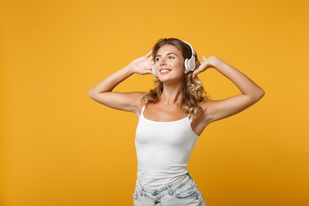 Mooie jonge vrouw meisje in lichte casual kleding met koptelefoon poseren geïsoleerd op geel oranje achtergrond, studio portret. Mensen levensstijl concept. Bespotten kopie ruimte. Muziek luisteren, dansen.