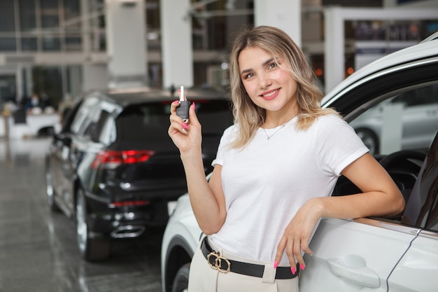 Mooie jonge vrouw met autosleutel, leunend op haar nieuw gekochte auto