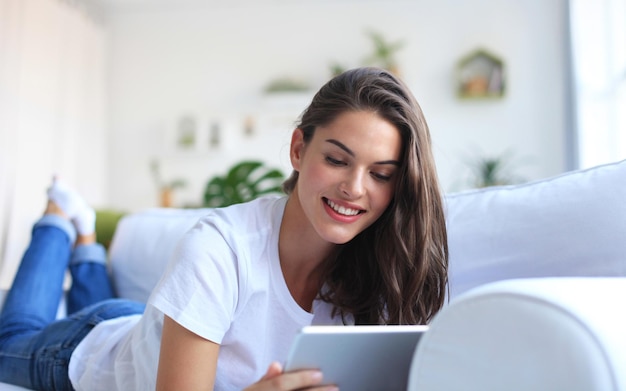 Mooie jonge vrouw met behulp van tablet zittend op de Bank thuis in de woonkamer.