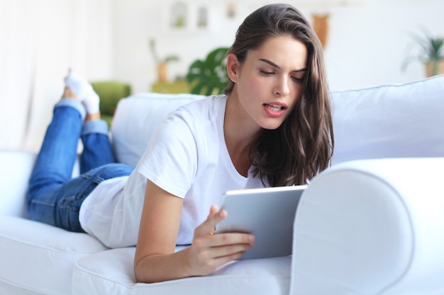 Mooie jonge vrouw met behulp van tablet zittend op de bank thuis in de woonkamer.