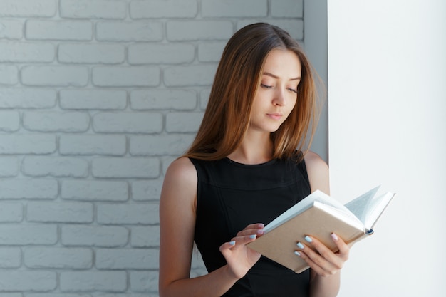 Mooie jonge vrouw met boek dichtbij bakstenen muur.