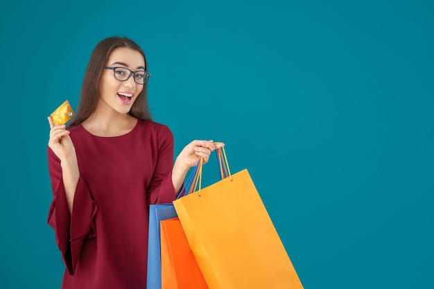 Mooie jonge vrouw met boodschappentassen en creditcard op kleur achtergrond