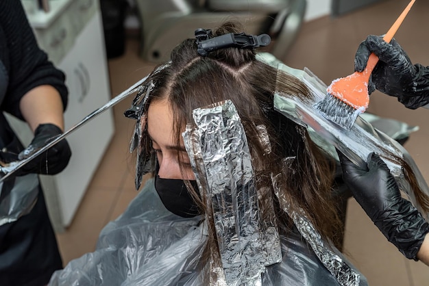 Mooie jonge vrouw met donker haar verlicht haar speciale middelen voor het kleuren van krullen Het concept van haarverlichting in een elite salon