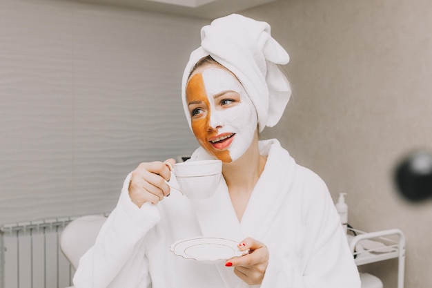 Mooie jonge vrouw met een gezichtsmasker drinkt koffie in het kantoor van schoonheidsspecialisten
