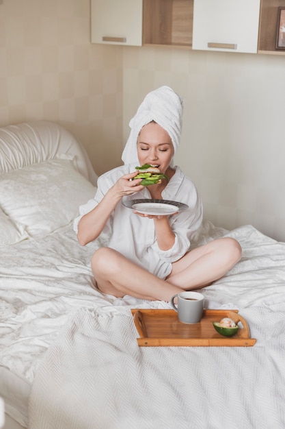 Mooie jonge vrouw met een handdoek op haar hoofd in bed die gezond ontbijt eet