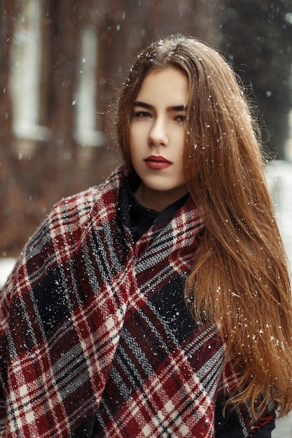 Mooie jonge vrouw met een sjaal in het sneeuwweer op eerste kerstdag