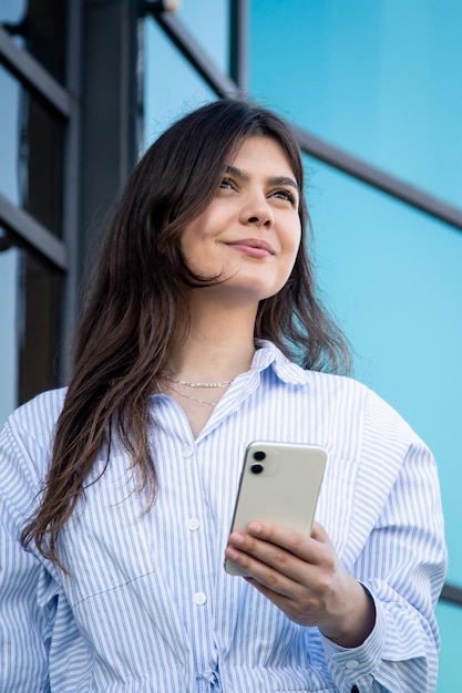 Mooie jonge vrouw met een smartphone op de achtergrond van een glazen gebouw