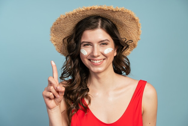 Mooie, jonge vrouw met een strohoed brengt zonnebrandcrème aan op haar gezicht