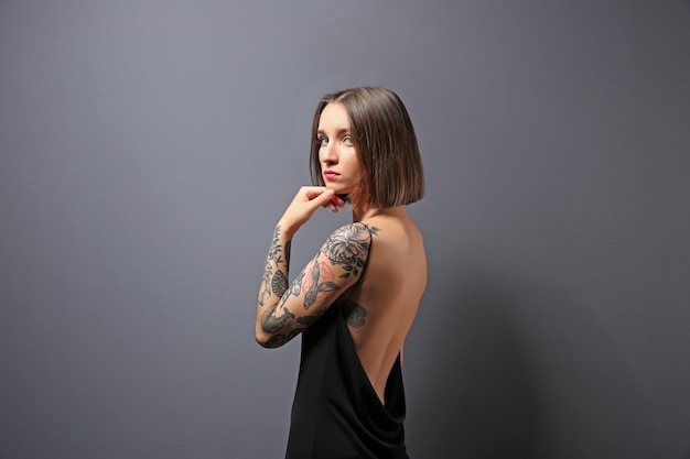 Mooie jonge vrouw met een tatoeage die zich voordeed op grijs