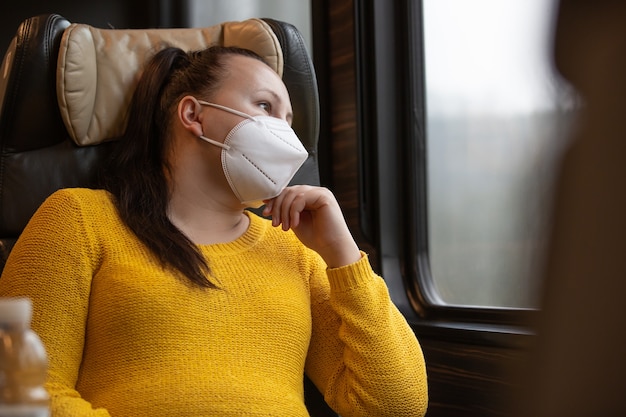 Mooie jonge vrouw met gezichtsmasker ook een beademingsapparaat dat met de trein reist tijdens pandemie covid-19, coronavirus, transportconcept