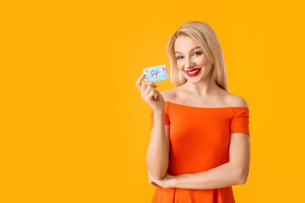 Mooie jonge vrouw met gift card op kleur oppervlak