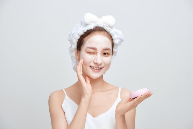 Mooie jonge vrouw met handdoek om haar hoofd gewikkeld die gezichtsmasker toepast