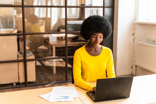 Mooie jonge vrouw met het afro-kapsel die op kantoor werkt
