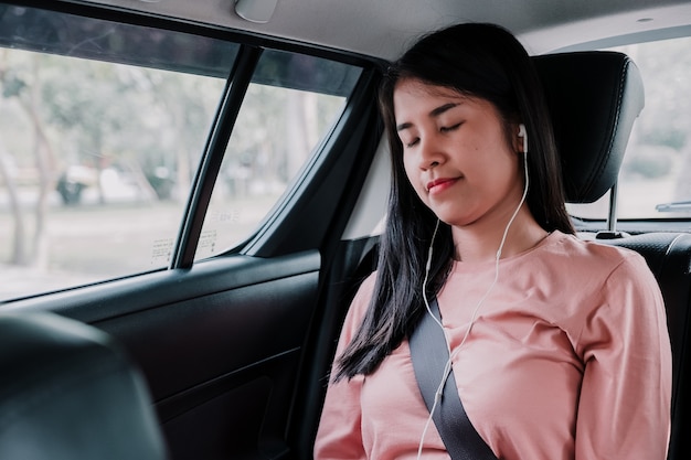 Mooie jonge vrouw met hoofdtelefoon die aan muziekslaap luisteren in auto.