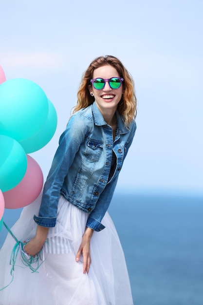 Mooie jonge vrouw met kleurrijke ballonnen aan zee