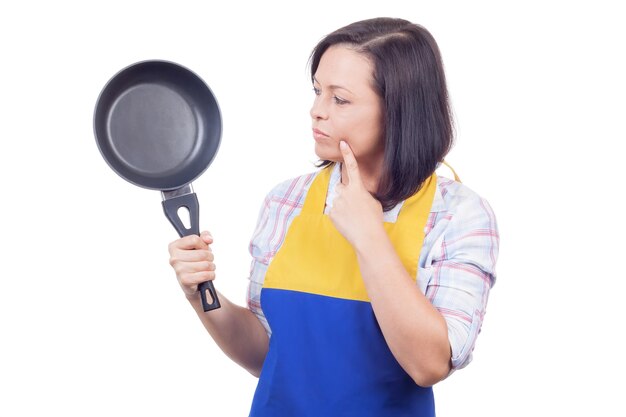 Mooie jonge vrouw met koekenpan denken wat te bereiden voor het diner op een witte achtergrond