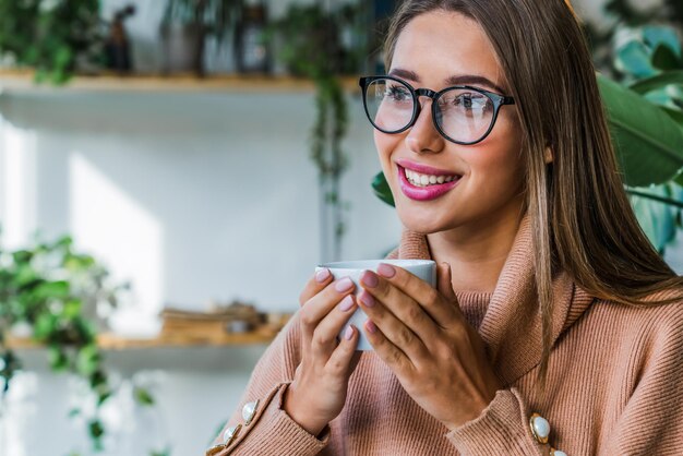 Mooie jonge vrouw met koffiekop die pauze neemt en droomt terwijl ze wegkijkt naar coffeeshop