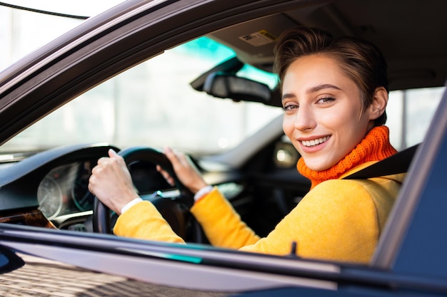 Mooie jonge vrouw met kort haar rijdt auto in de stad