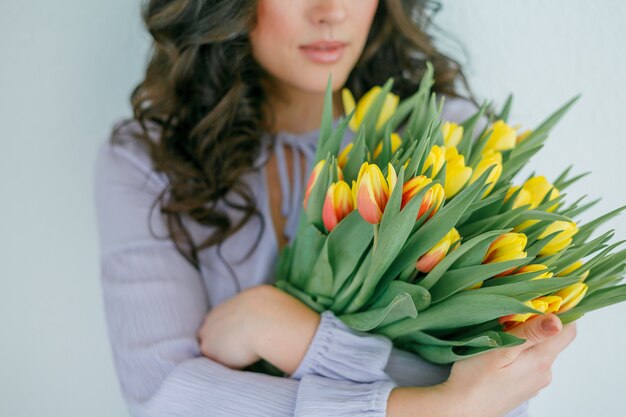 Mooie jonge vrouw met krullend haar houdt een boeket tulpen.