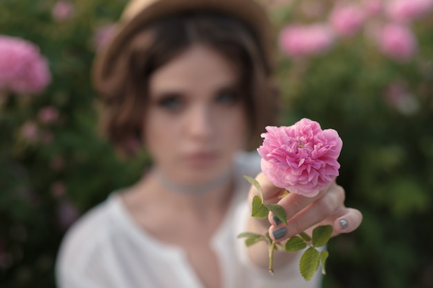 Foto mooie jonge vrouw met krullend haar poseren in de buurt van rozen in een tuin. het concept van parfumreclame.