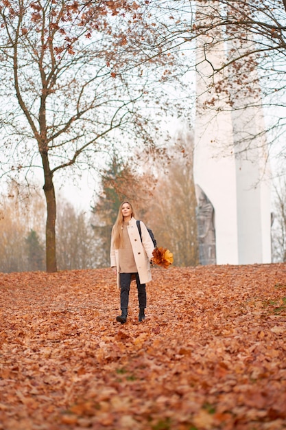 Mooie jonge vrouw met lang blond haar, gekleed in stijlvolle outfit met boeket