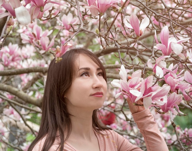 Mooie jonge vrouw met lang haar die omhoog kijkt naar bloeiende boom met roze magnoliabloemen