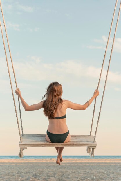 Mooie jonge vrouw met lang haar in zwembroek op touw zwaait hoog in de lucht magisch licht van zonsondergang verticaal frame achteruitzicht